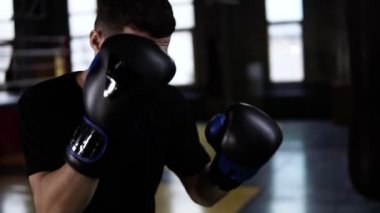Siyah T-shirt, tespit boksör yapmak adam boks torbasına spor salonunda kapalı vurur. Avcı tek başına ağır çekimde eğitim