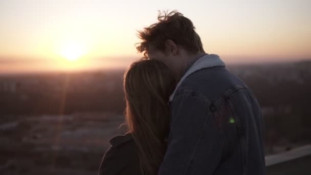 Прекрасна сцена молодої колючки на даху під час заходу сонця. Чоловік йде і приєднується до своєї дівчини ззаду, зупиняючись на горизонті. Усміхнена пара насолоджується романтичними моментами разом — стокове відео