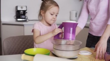 Güzel genç anne ve pasta birlikte hazırlanıyor şirin küçük kızı. Küçük kız evde mutfak un elek altı kullanıyor