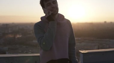 Esmer çocuk rahat objektif mercek parlamaları çatıda duran ve onun smartphone kullanarak arama. Söz, gülümseyen ve güneş ışınları el ile üzerinden gizle