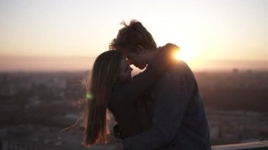 -Uzun saçlı kız ve blondy adam arka planda sunrising güzel bir manzara ile kucaklayan rüzgarlı çatıda ayakta millenial Romantik Çift