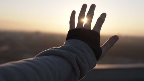 Mano de hombre tocando la luz del sol a mano sobre el hermoso fondo del cielo mientras está de pie en el techo. Hombre feliz mirando el amanecer a través de sus dedos. Movimiento lento — Vídeos de Stock