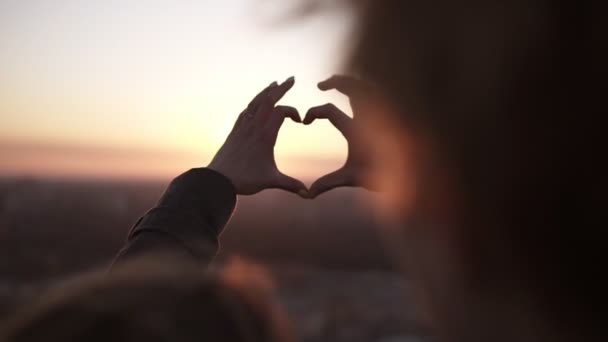 Romántica pareja joven unir las manos en forma de corazón contra el sol de pie en el techo. Amor y afecto, citas en el techo — Vídeos de Stock