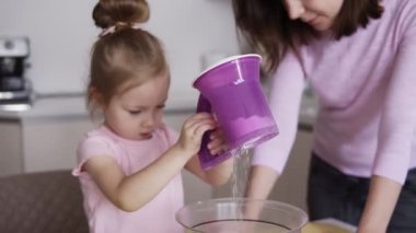 Tatlı kızı annesi mutfak yardımcı oluyor, elek ve kase içinde malzemeyi karıştırma ile unu ekleyin. Esmer kadın yönetmek için yardım. Hareket ekmek