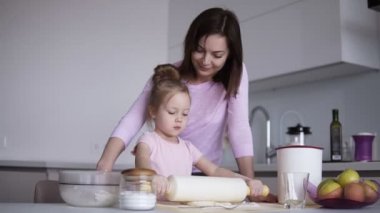 Beyaz genç sevgi dolu anne sevinçle birlikte mutfakta yemek yaparken bir oklava ile hamur yayıyoruz sevimli küçük kızını yardım