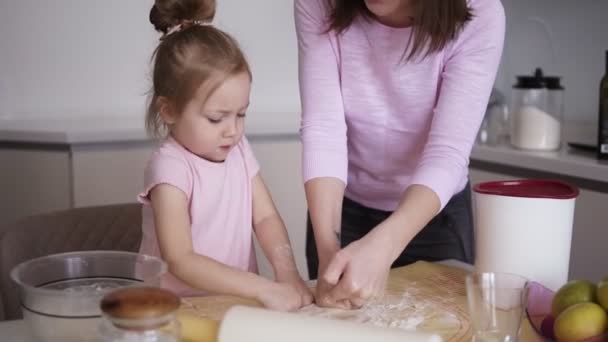 Όμορφη νεαρή μητέρα και την κόρη της χαριτωμένο μικρό σχηματίζουν τη ζύμη πάνω στο τραπέζι με τα χέρια στην κουζίνα στο σπίτι. Αργή κίνηση — Αρχείο Βίντεο