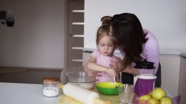 Pembe gömlek kase un annesi üzerinde kendi mutfak ile karıştırma, küçük kız. Sweet aile. Sevgi dolu bir anne kızı öper. Birlikte, çocuk, Aile içi yaşam ile pişirme yemek