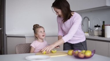 Anne ve kızı evde sağlıklı yemek pişirme ve eğleniyor. Genç kadın masanın üstüne sarı elma önünde kızı kesme. Yardım, ev içi, ekip çalışması annelik kavramı