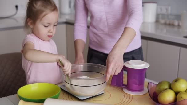 Malá holčička v růžové košili smíchání mouky v míse s matkou na jejich kuchyni. Vaření, pečení s dítětem, domácí život — Stock video
