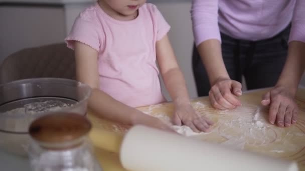 Mãe alegre com seu filho, uma menina se divertindo enquanto prepara um bolo em sua cozinha moderna e branca. Eles jogam palmas com farinha — Vídeo de Stock