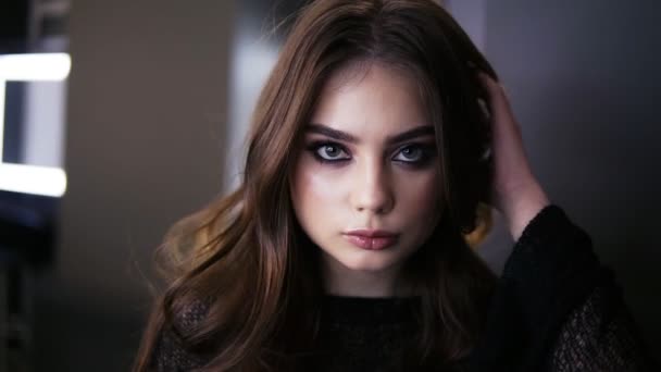 Portrait of a young beautiful girl looks to the camera and straightens her fair hair in professional makeup studio, girl is getting ready for a date. Perfect makeup. Front view — Stock Video