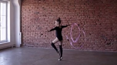 Ritmik Jimnastik: kız siyah vücut Studio windows ve tuğla duvar arka plan jimnastik okulda jimnastik egzersiz pembe bir kurdele ile gerçekleştirmek. Egzersiz, ağır çekim