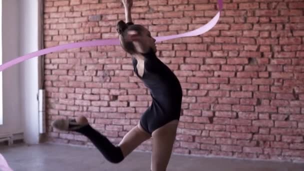 Imágenes en cámara lenta de la pequeña gimnasia en negro girando la cinta mientras se hace el ejercicio de gimnasia en el estudio — Vídeo de stock