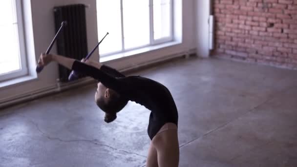 Jonge turnster doen cirkel met mace op de benen in de studio op venster en bakstenen muur op de achtergrond. Slow motion beelden — Stockvideo