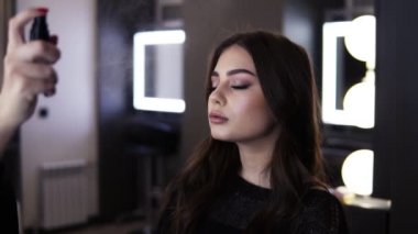 Makyaj sanatçısı siyah at kuyruğu ile sprey bitirme a yapmak kullanır ve yavaşça bir mesafeden istemcileri yüzünde spreyler. Bitmiş makyaj ve hairso ile siyah elbiseli güzel genç bayan