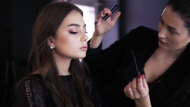 Maquillaje artista haciendo maquillaje profesional de mujer joven con el pelo largo en vestido negro. Rímel que se aplica sobre pestañas largas con cepillo de rímel. Extensiones de pestañas. Maquillaje para ojos verdes — Vídeo de stock