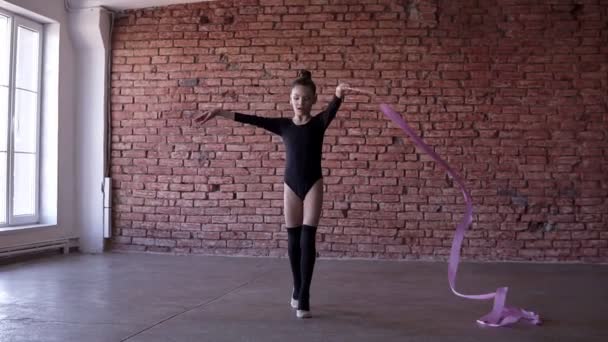 Retrato de gimnasia elegante girando con cinta rosa delante de la cámara en el estudio con el fondo de la pared de ladrillo rojo. Movimiento lento — Vídeo de stock