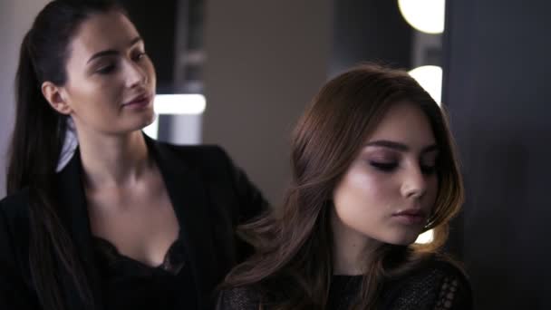 Artista de maquillaje femenino con un cabello oscuro y una joven dama mirando al espejo y admirando el trabajo de maquillaje en un salón de belleza. Un look perfecto. Estudio de maquillaje profesional — Vídeo de stock