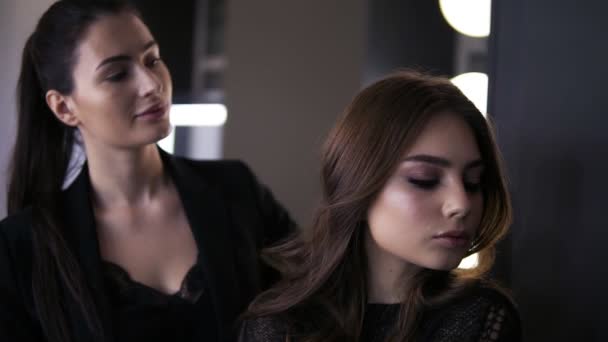 Maquilleuse aux cheveux foncés et jeune femme regardant le miroir et admirant le maquillage dans un salon de beauté. Parfait. Studio de maquillage professionnel — Video