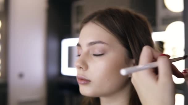 Visagist legt laatste hand van eyeshadows op de oogleden van het model. Lichte make-up studio. Close-up beelden — Stockvideo