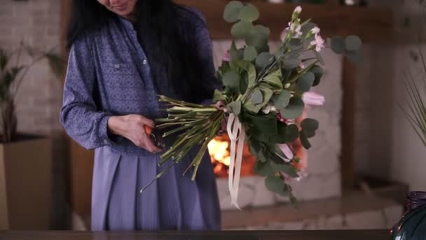 女性花屋花束の花の茎をカットします。青いドレスの女性は完璧な花束を組み立てます。最後の仕上げ: 花束の準備が整う前に茎をカットする必要があります。背景に Firelace — ストック動画