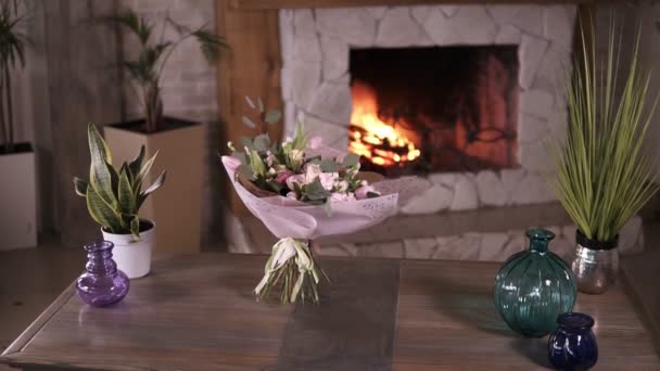 Schöner Strauß pastellfarbener Blumen in rosa Zierpapier steht nach dem Blütenmeisterkurs an den Stängeln auf einem grauen Tisch. Blumen Dekoration Design-Konzept. Kamin im Hintergrund — Stockvideo