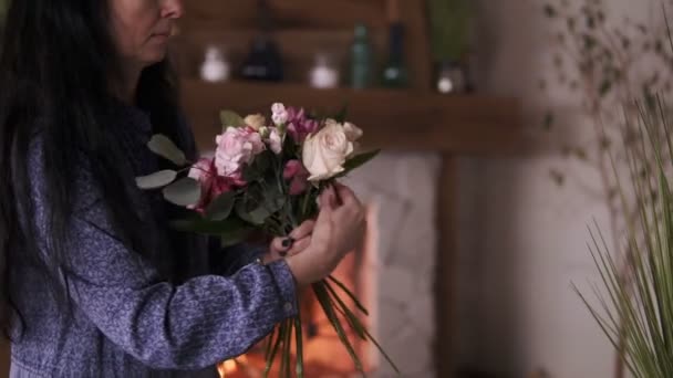 Florista no trabalho: mulher adulta morena bonita fazendo moda buquê moderno de flores e plantas diferentes em estúdio em casa. Vista lateral — Vídeo de Stock