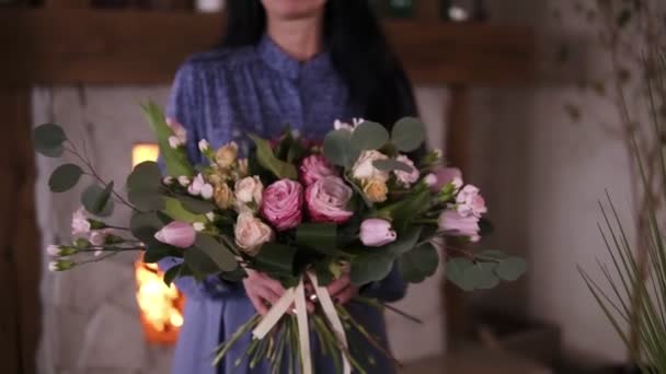 Mujer profesional artista floral, florista en vestido azul perfuma el ramo hermoso hecho a sí mismo de diferentes rosas y hojas en el taller, tienda de flores o estudio en casa. Floristería, artesanal y pequeña — Vídeo de stock