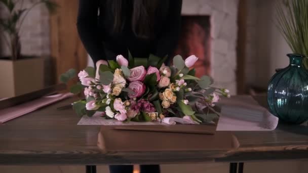 Professional woman floral artist, florist wraps flowers - pink roses in gift paper at workshop, home studio. Floristry, handmade and small business concept. Slow motion — Stock Video