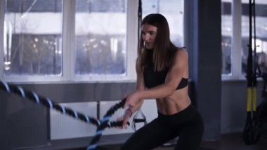 Güçlü kas kadın ile savaş ipler çalışma dışarı. Görüntüleri siyah spor salonunda çekici bir kadın. Ağır çekim