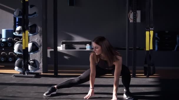 Profi im Sport. Vorderansicht einer schönen jungen Frau in Sportbekleidung, die Stretching macht, während sie auf dem Boden in einer dunklen, modernen Sporthalle liegt — Stockvideo