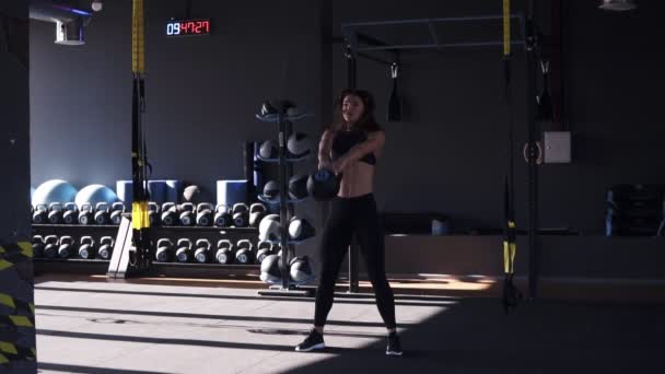 Pełna długość dziewczynka fitness w sportowej robi treningu crossfit z 10 kilo czajnik dzwon. Wysokiego podnoszenia pod głowę kettlebell duży, czarny z wyciągniętymi rękami. Sportowy, wyposażenie siłowni — Wideo stockowe