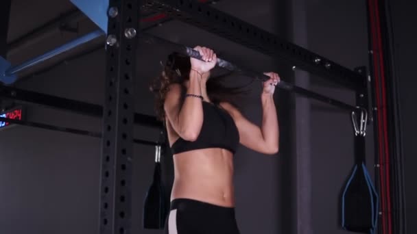 Вид сбоку на мускулистую взрослую спортсменку в черных леггинсах и бюстгальтере, висящую на металлическом баре в тренажерном зале и детерминированную на подбородке — стоковое видео