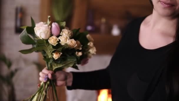 Longo florista feminino segurando um buquê meia feita e adicionando flores e plantas para a composição. Projetando, oficina floral, lazer. Imagem borrada da lareira no fundo — Vídeo de Stock