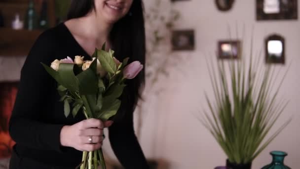 Mulher branca e sorridente florista profissional segurando um buquê meio feito e adicionando flores e plantas à composição. Projetando, oficina floral, lazer. Imagem borrada da lareira no — Vídeo de Stock