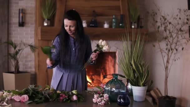 Mujer adulta de pelo largo dedicada a la florística comienza a recoger las mejores flores para su composición de flores. Elegir los racimos de la variedad de flores en la mesa — Vídeos de Stock