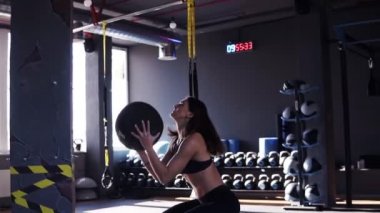 Arka planda ekipman dolu koyu renkli modern bir spor salonunda bir duvara bir ilaç topu atarak egzersiz genç bir fit kadın Sideview görüntüleri