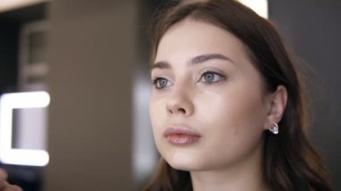 Tanınmaz makyaj sanatçısı genç kadın yüz üzerinde sert temel uygulayarak. Salonda profesyonel makyaj. Görüntüleri kapatın. Yavaş çekim çekimi