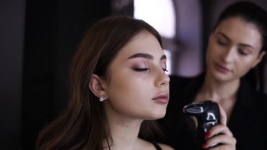 Airbrush ile makyaj işlemi sırasında genç güzel kız yüzü. Güzel esmer kadın sanatçı bir model için mükemmel bir yüzey cilt yapar. Kusursuz makyaj eğitimi