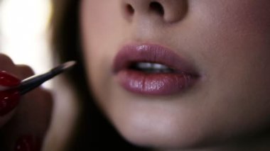 Son derece yakın görüntüleri makyaj sanatçısı dudakları genç kadın fırça ile ruj uygulayarak. Makyaj modeline proses uygulaması dudak parlatıcısı