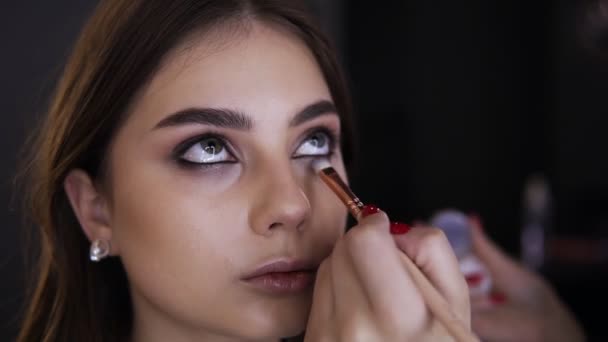 Retrato de mujer joven mientras que los ojos del maquillaje en el estudio cosmético. Maquillaje artista que utiliza cepillo para aplicar sombra de ojos brillante en el párpado bajo. Maquillaje elegante, concepto de belleza — Vídeo de stock