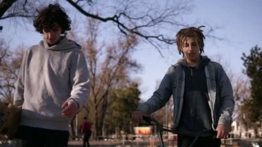 İki arkadaş kaykaycı ve bmx binici birlikte şehir paten parkı yürüyor. Arkadaşlar paten parkında iletişim kurarlar. Güneşli bir gün. Aktif boş zaman. Ön görünüm