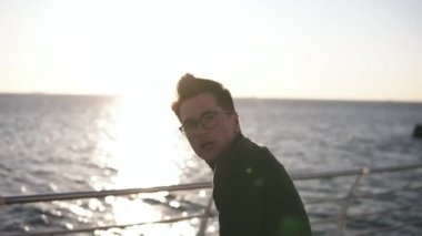 Siyah ceketli ve sahilde gözlüklü genç bir adam sabah güneşinde dans etmeyi pratik etti. Açık havada açık havada açık havada dans eder. Yavaş çekim