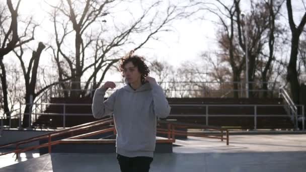 Im Freien hübsche junge Männer Porträt. Teenager-Junge im Kapuzenpulli läuft über den Skatepark mit Naturhintergrund. Typ, der selbstbewusst geht, die Kapuze aufsetzt. Zeitlupe — Stockvideo