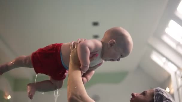 Giovane madre con bambino che nuota in piscina coperta godendo. Mamma felice con amore giocare con il figlio del bambino a piscina - lo solleva sopra la testa — Video Stock