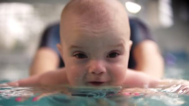 Mãe ou treinador de natação em traje de natação especial mantém a criança acima da água e leva-o através da superfície na piscina. Close up de babys rosto — Vídeo de Stock