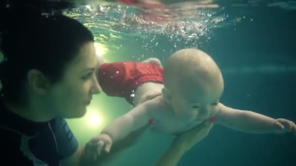 Mãe morena com bebê filho mergulho subaquático com diversão na piscina. Estilo de vida saudável, pai ativo, aulas de natação em piscina interior com criança. Filmagem acima e abaixo da água — Vídeo de Stock