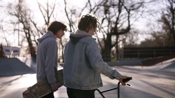 Deux amis skateboarder et bmx rider marchent ensemble dans le skate park de la ville. Les amis communiquent dans le skate park. Journée ensoleillée. Temps libre actif — Video