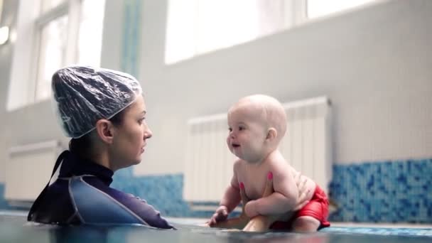 Anne ya da eğitmen o ne yapacağını kapalı yüzme havuzu kenarında oturan küçük bebek çocuk açıklar. Altında dalış için suya çocuk itin — Stok video