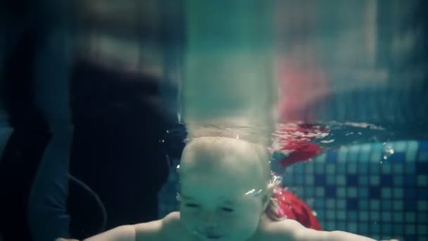 Sevimli mutlu yürümeye başlayan çocuk yüzme havuzunda suyun altında dalış ve annesi onu çıkmak için yardımcı olana kadar orada yüzme. Bir sualtı atışı. Bebek yüzünün yakın çekim — Stok video